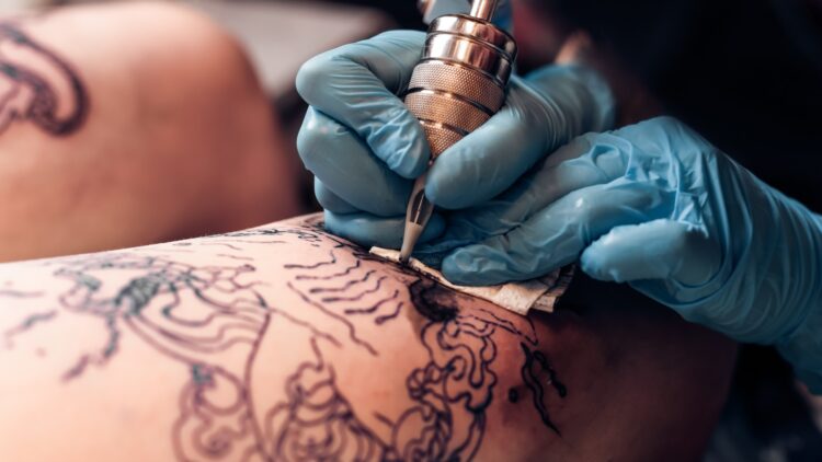 Closeup tattoo artist fill circuit tattoo in a professional salon. Leg with a pattern and black paint. Master works in black sterile gloves. SSUCv3H4sIAAAAAAAEAJ2RTW6EMAyF95V6B5Q1keIQAulVqi6Mk5lGZcgIwlTViLs3/FVZd8f77Eee7efrS1GwDidP7K14ripp3/fzFEeMPgwJi/LgzvoYRo/9Cle2bBU2RYzz5Kb1FwcijO6aend4+M933nddnIWtmBypxFiZsWnuNnaipfy3c//4OEfBqxvoZwucDTK63uE+yJGRXcAQaCQusAaupCLeSSKuldYXaMFo6M6XGRiLjTYth1qkZtAV7yrb8ooQO2yMEWj/mgXY2kgUXDa14UpJ4i0mh9ItkDRCqRa3/Hto9vUd3XjLl/zw1oVM42x9yPb9CIT9aqiyGe+jJz9cM1uIn27Mb5eOH24ZGELcdnKsmNl03FVCBUJrAarRtRRKViblXX4BnITL3lQCAAA=